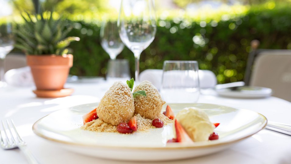 Erdbeerknödel auf Teller, umgeben von Erdbeerscheiben und dekorativem Minzblatt.
